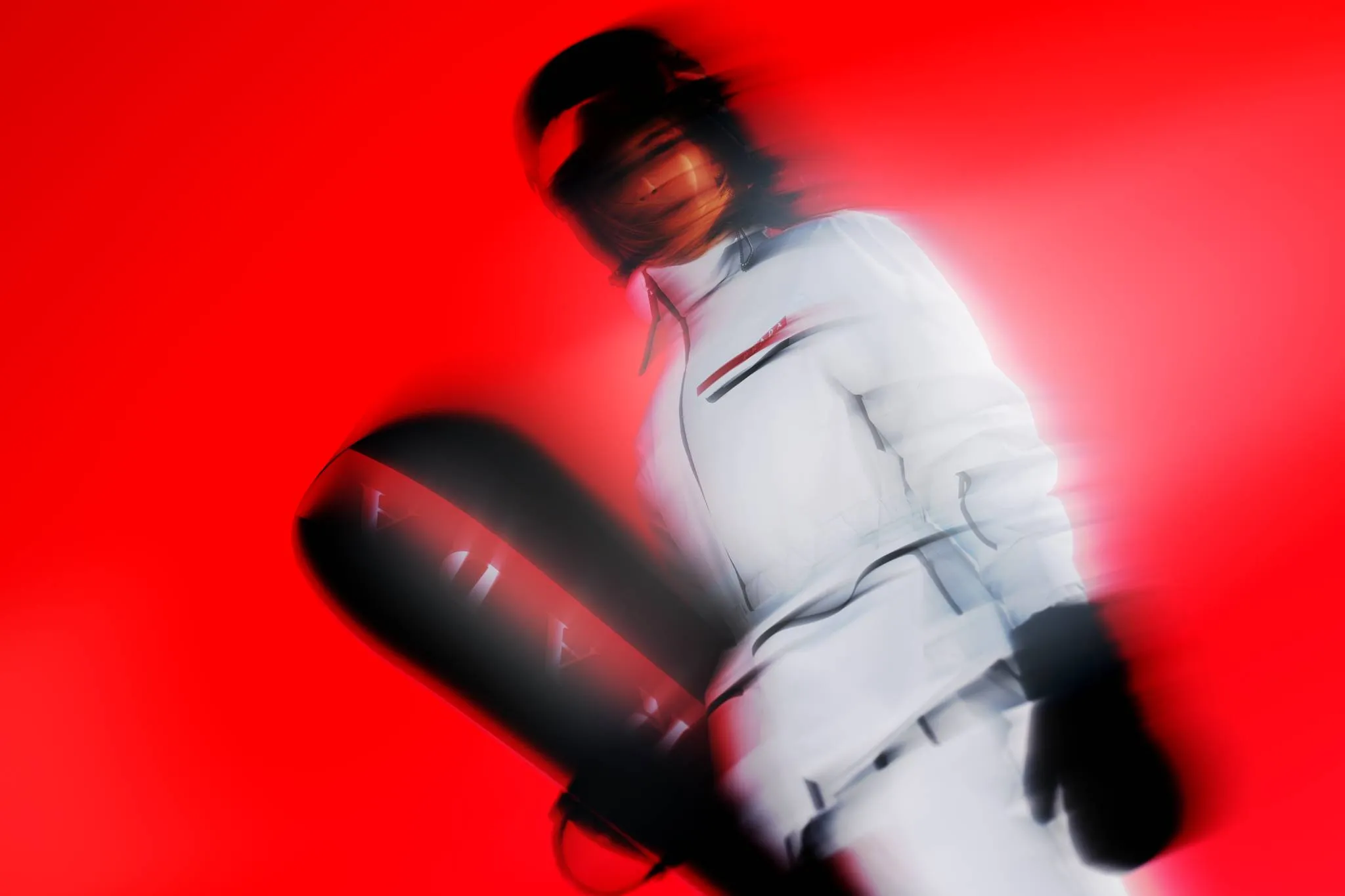Dynamic motion shot of a snowboarder in sleek white winter gear holding a black Prada snowboard, set against a vivid red background with artistic motion blur.
