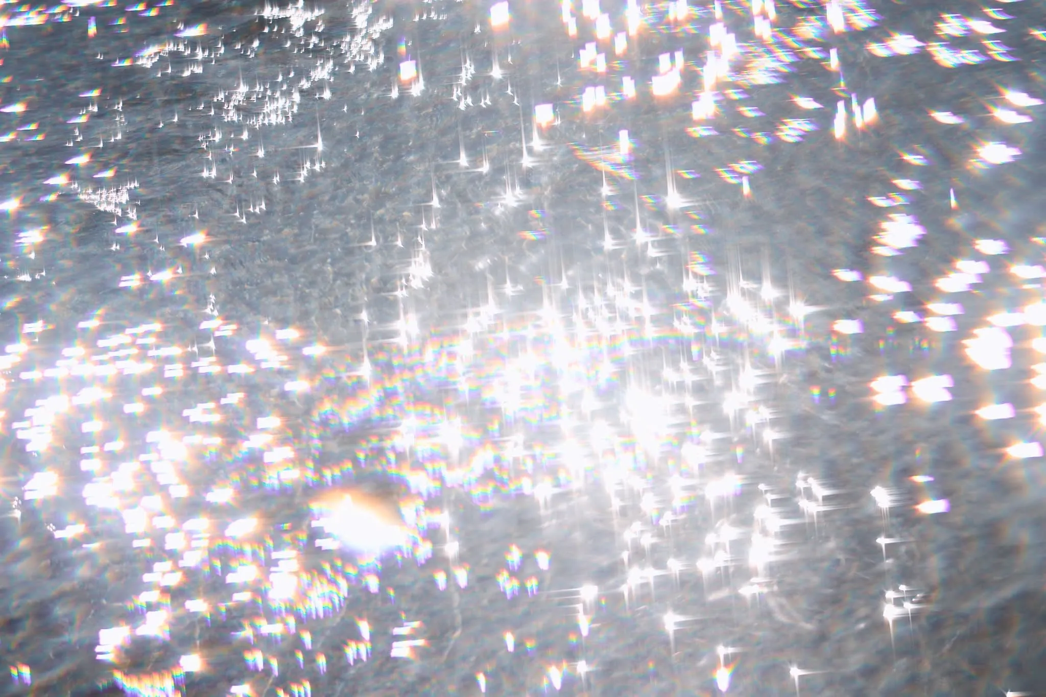 Sunlight reflecting off rippling water, creating a sparkling, prism-like effect with rainbow-colored highlights.