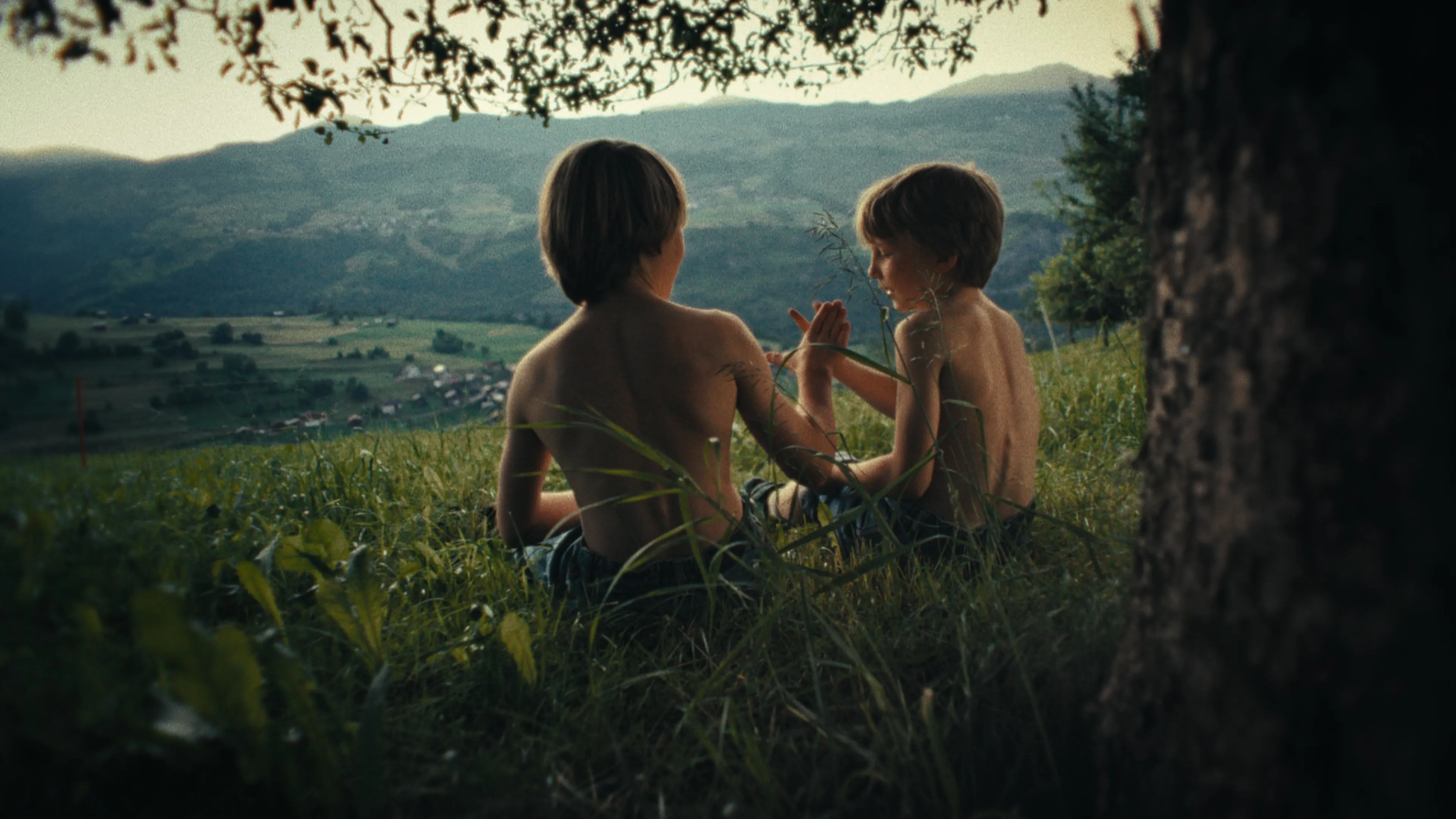 zwei Kinder sitzen unter einem Baum in Tersnaus, Graubünden. 