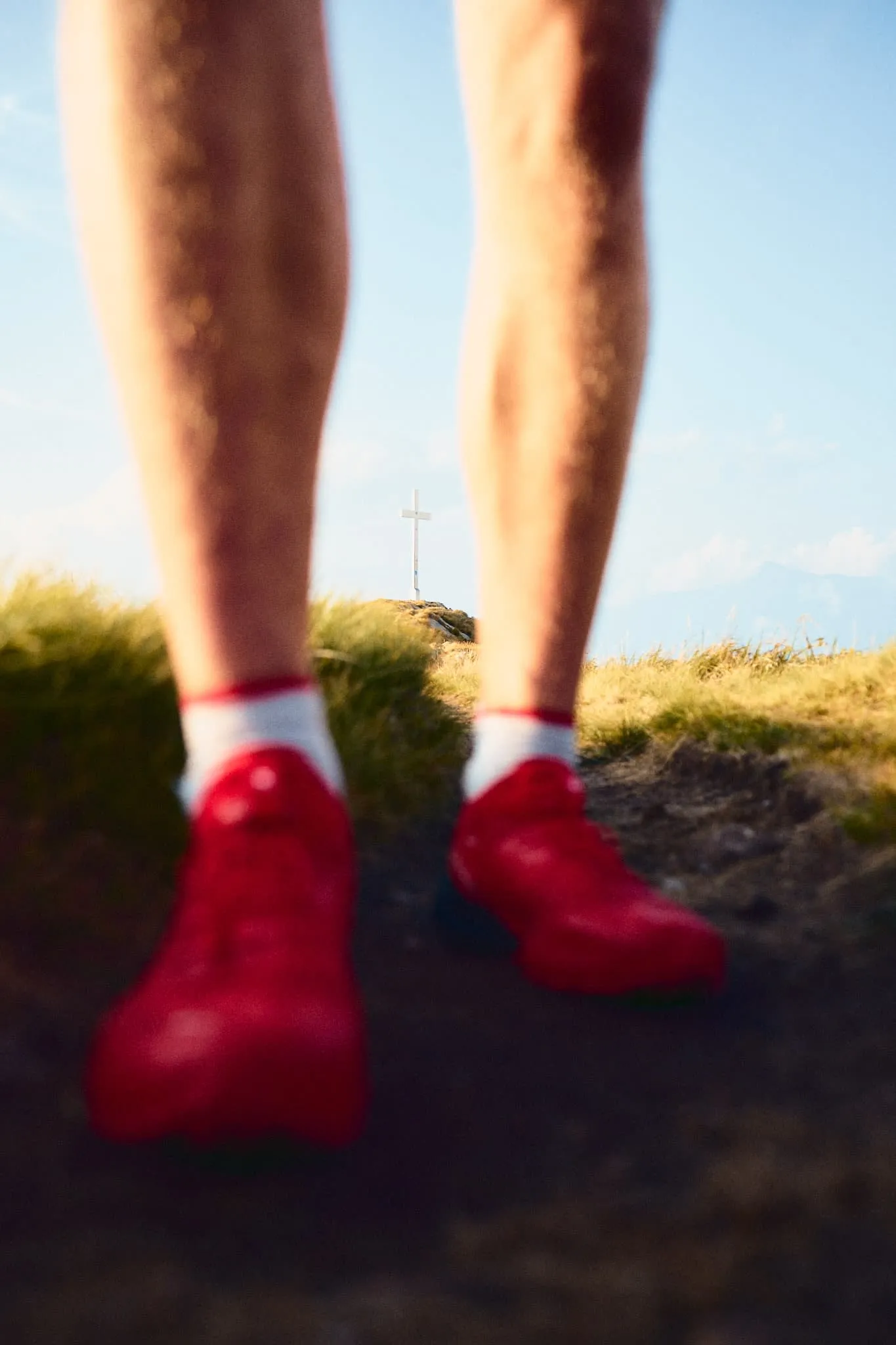 A clever low-angle focus where the legs and red shoes dominate the foreground, drawing attention to the distant cross centered between them — it creates a powerful sense of direction and purpose.