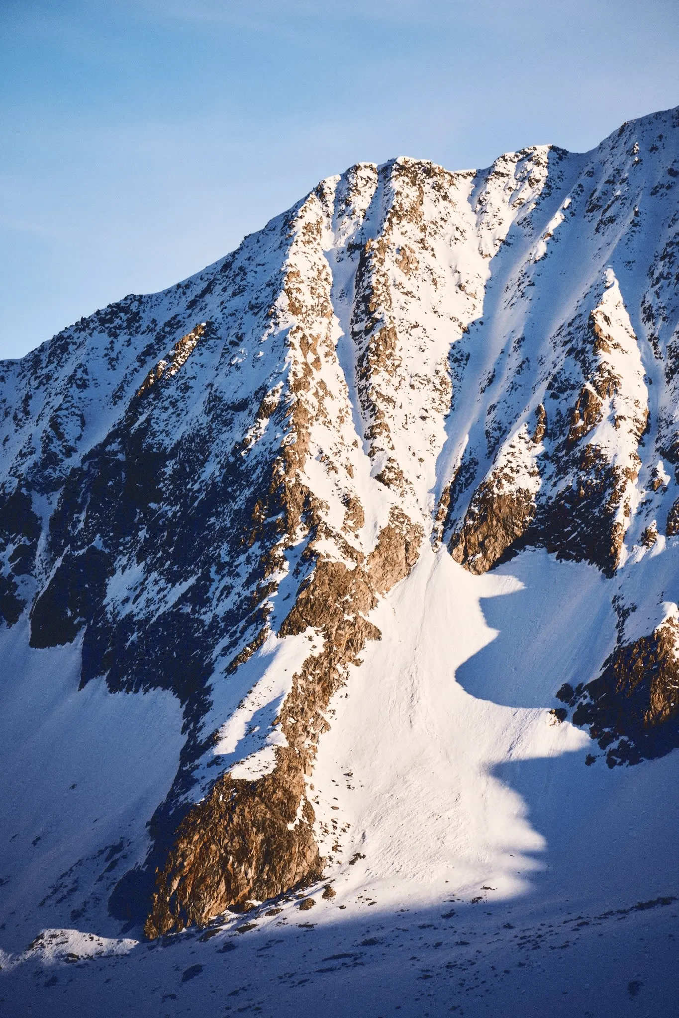 A wide landscape photograph capturing a rugged, mountainous terrain under soft daylight. The composition features layered peaks fading into the distance, with muted earth tones and gentle atmospheric haze creating a sense of depth and stillness.