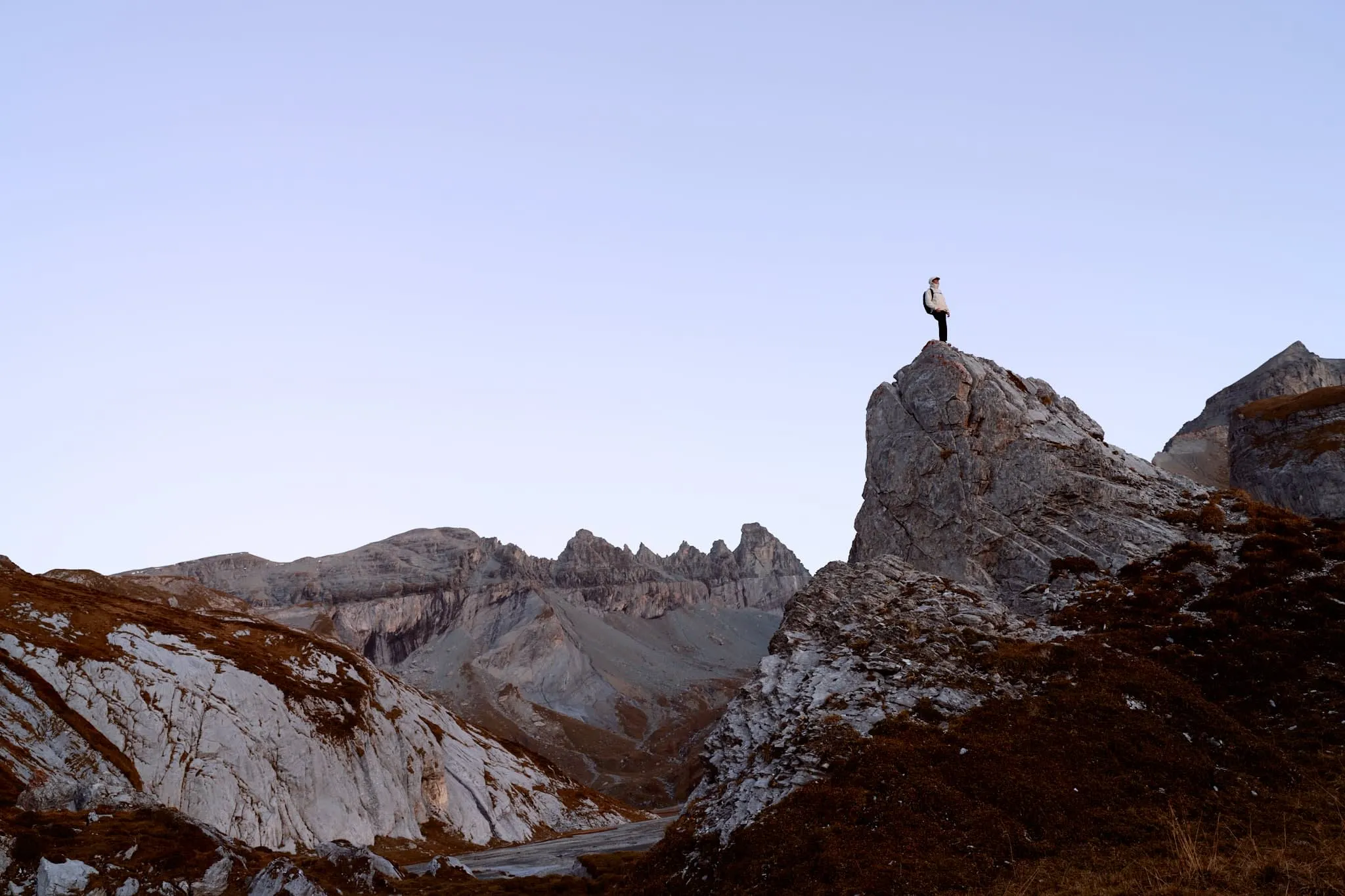"Adventurer standing confidently atop a jagged rock formation, surrounded by mountain peaks at golden hour."